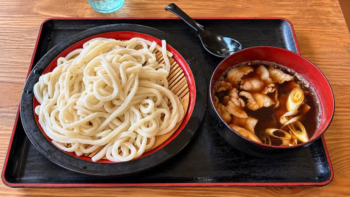 ざるに盛られた白いうどんと、豚肉やねぎが入った肉汁のつけ汁