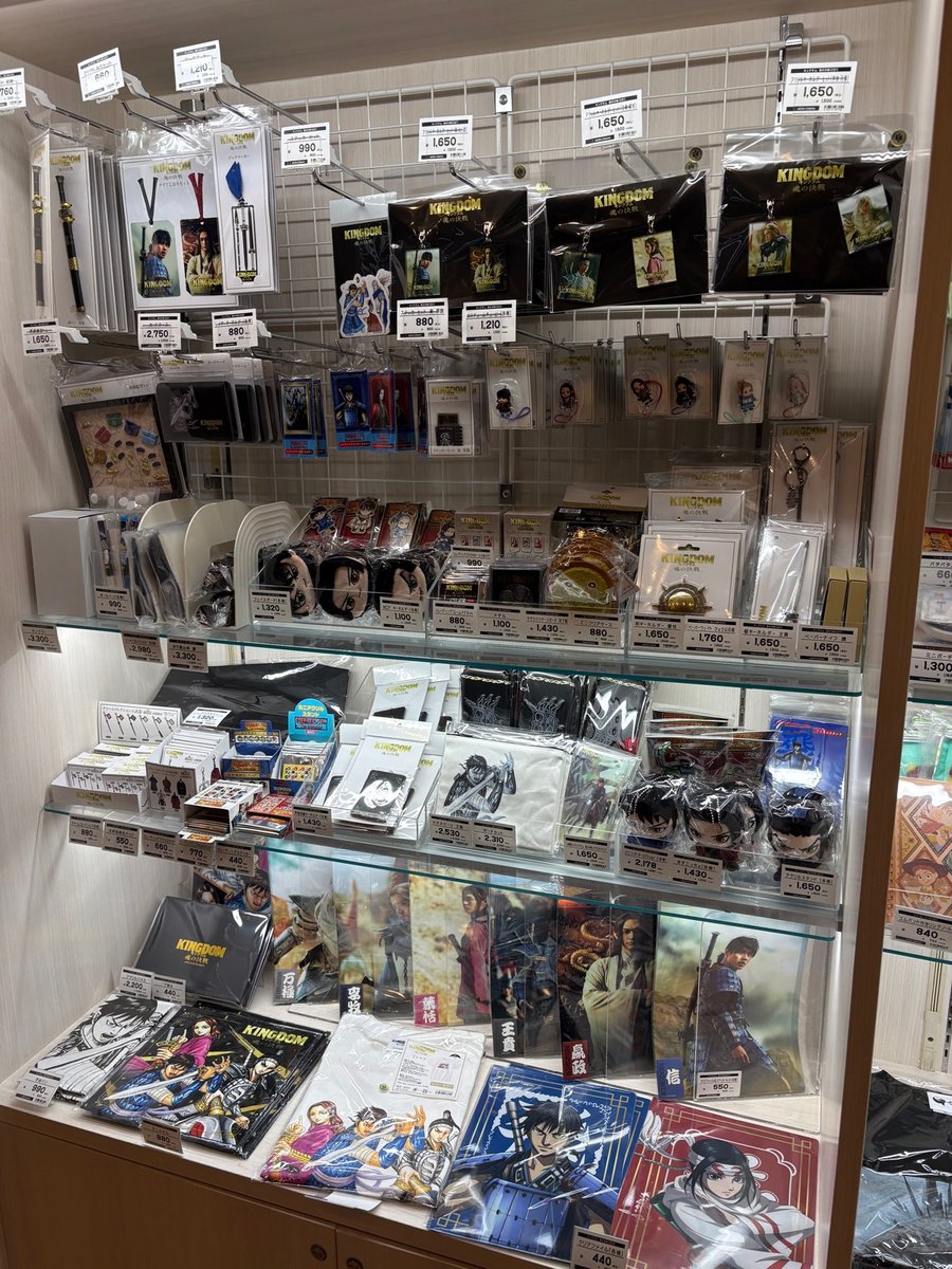 映画館のキングダム「魂の決戦」グッズ売り場。缶バッジやアクリルスタンド、クリアファイルなどがずらりと並ぶ棚
